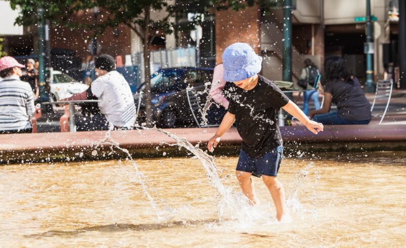 Summer heat in the city. Little boy playing in the water fountain making splashes. Staying cool