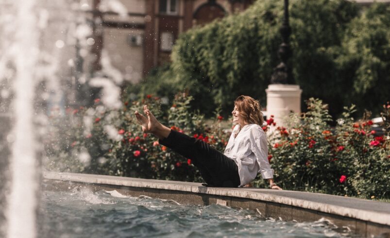 Young woman in hot summer having fun in the city fountain